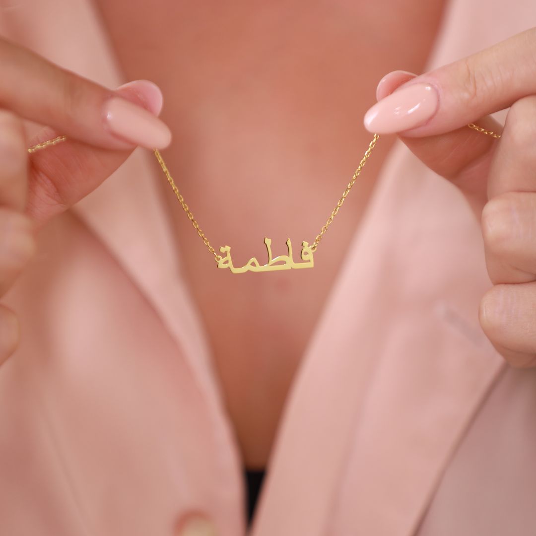 Gold-coloured Arabic name necklace pendant held in both hands