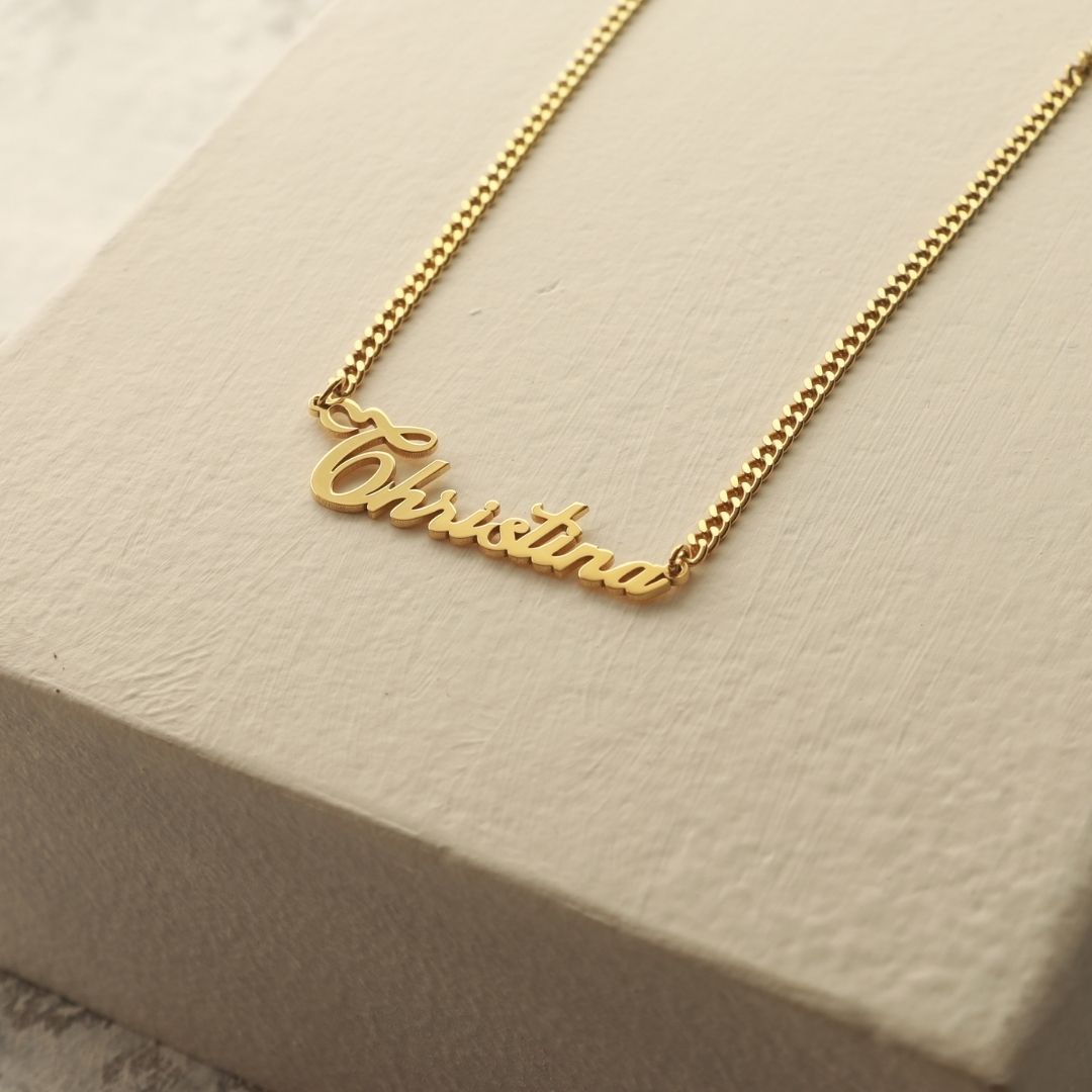 Gold-colour Christina name necklace on a curb chain displayed on a cream block