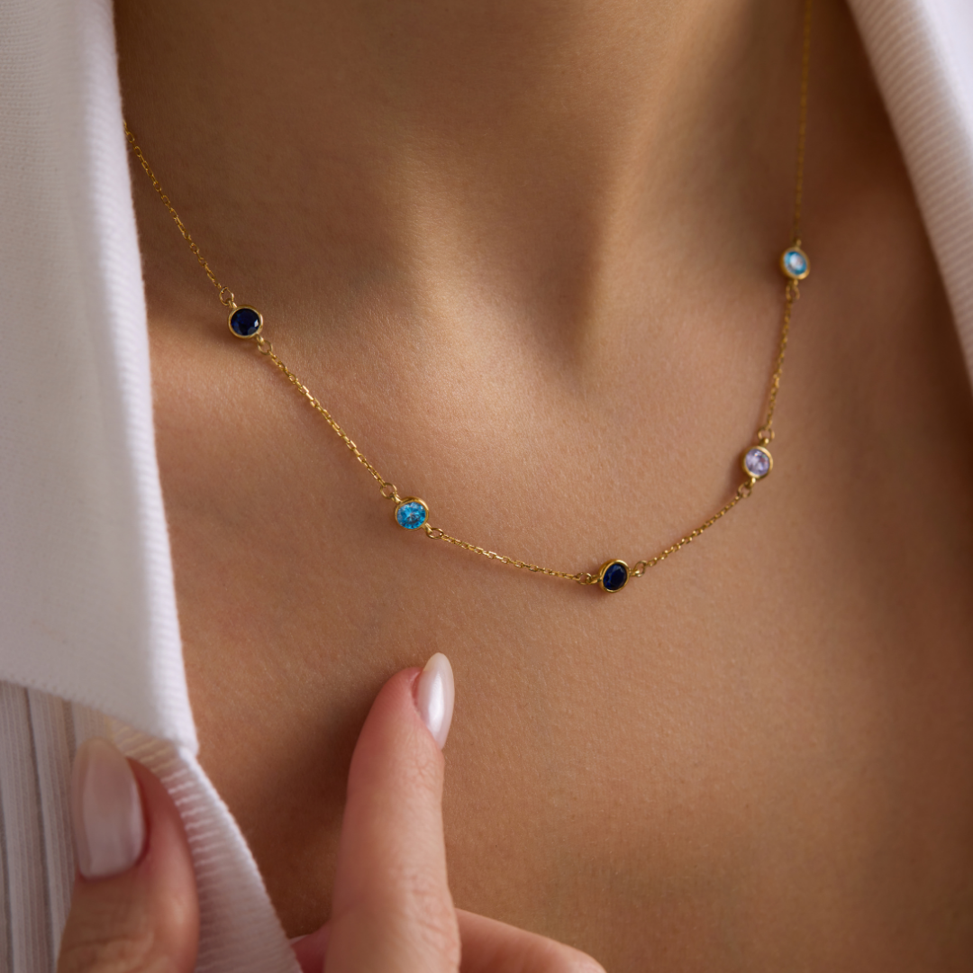 Gold-toned necklace with blue and purple birthstones worn with a white shirt