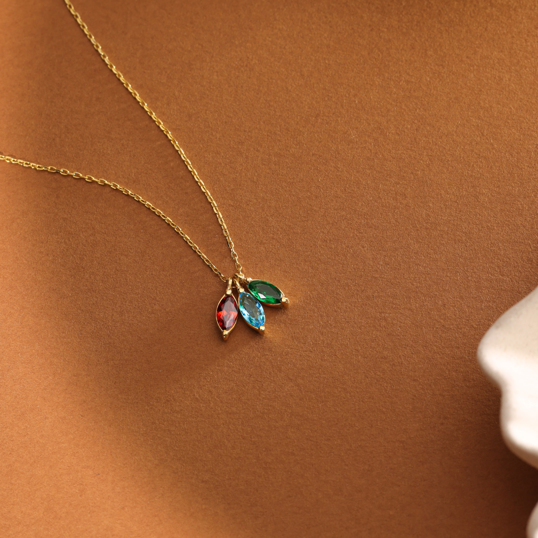 Family birthstone necklace with three coloured marquise-shaped charms on an orange surface