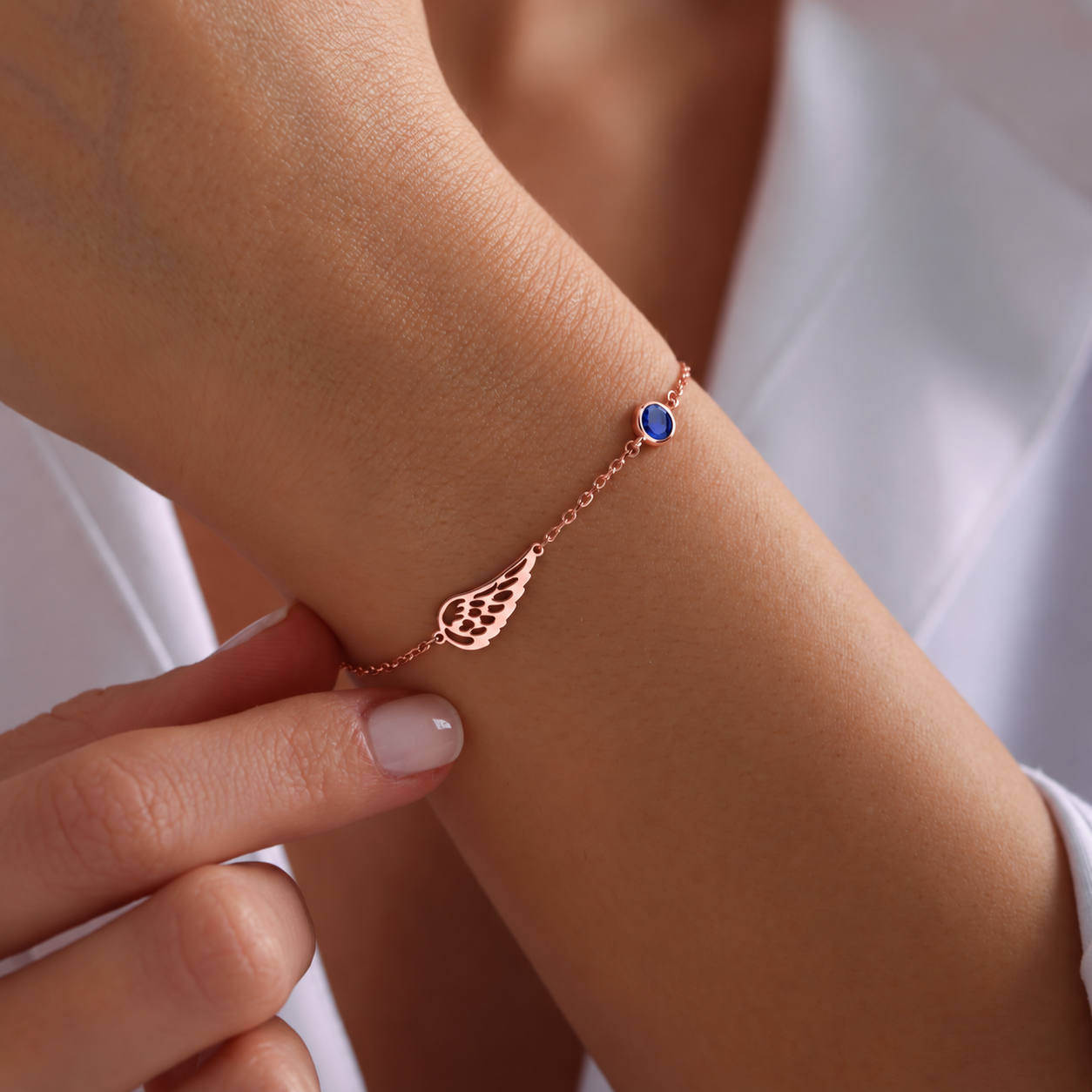 Angel wing bracelet in 14K rose gold filled with a blue birthstone, worn on the wrist