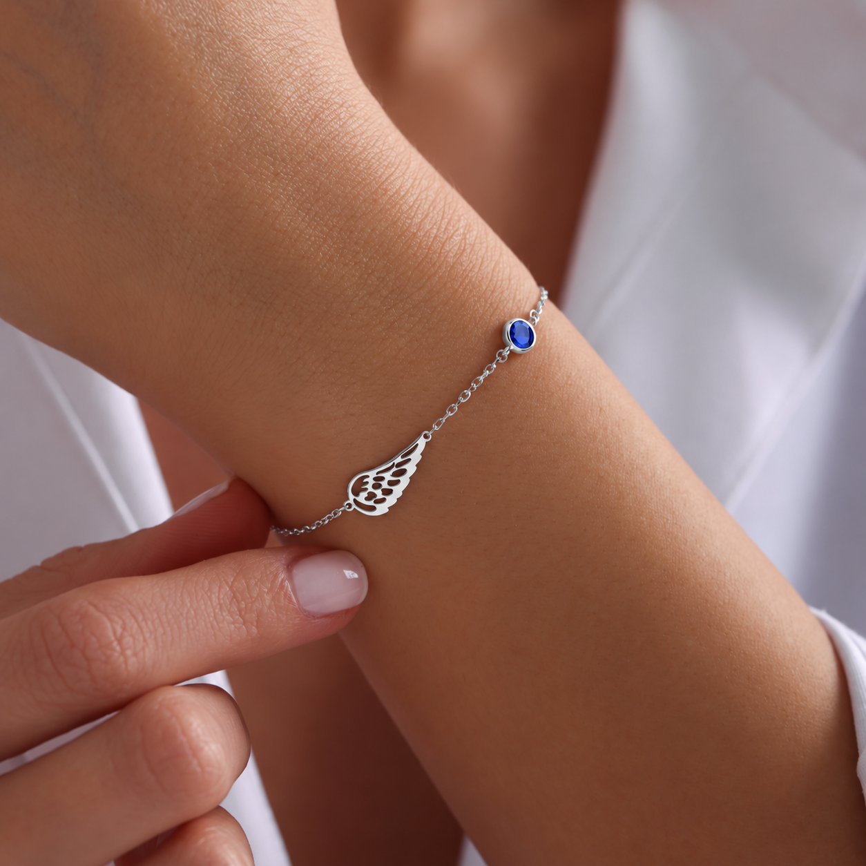 Angel wing bracelet in 14K solid white gold with a blue birthstone, worn on the wrist