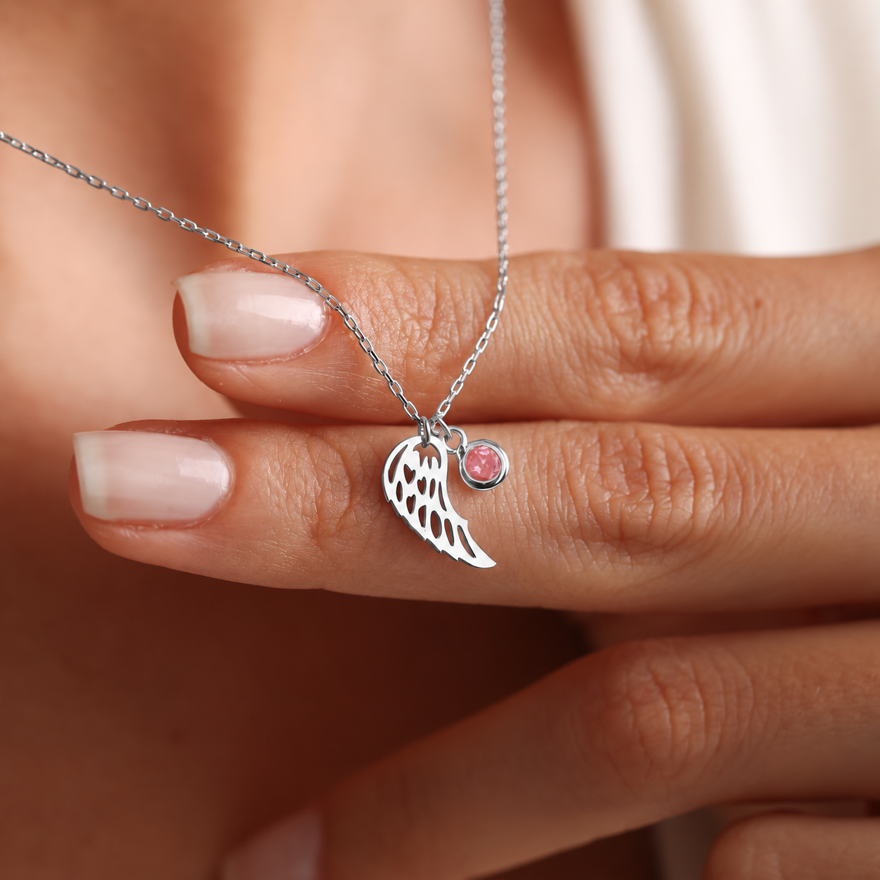 Angel wing birthstone necklace in sterling silver, with a pink gemstone held against the fingers