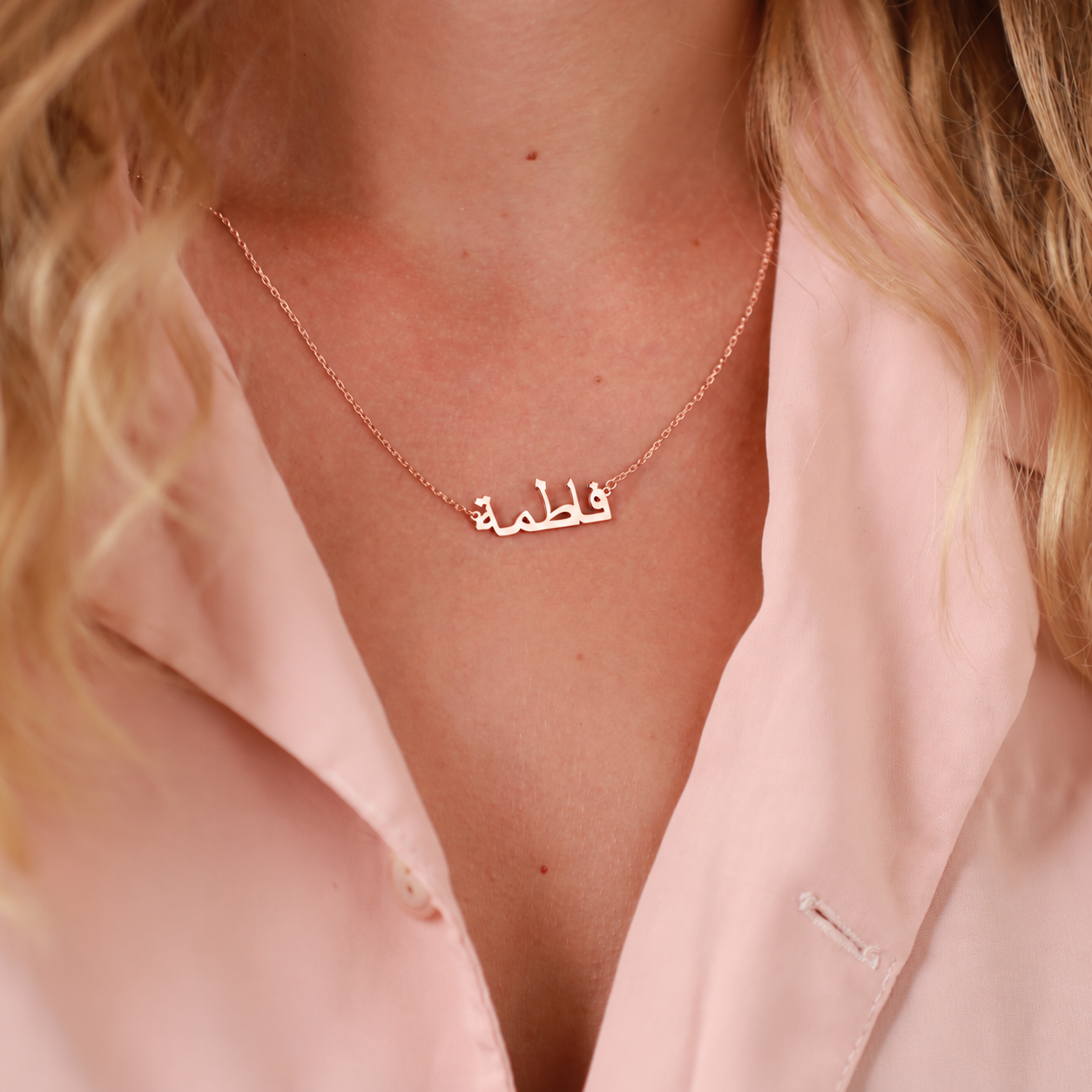 Personalized Arabic name necklace in rose gold, worn with a pink shirt