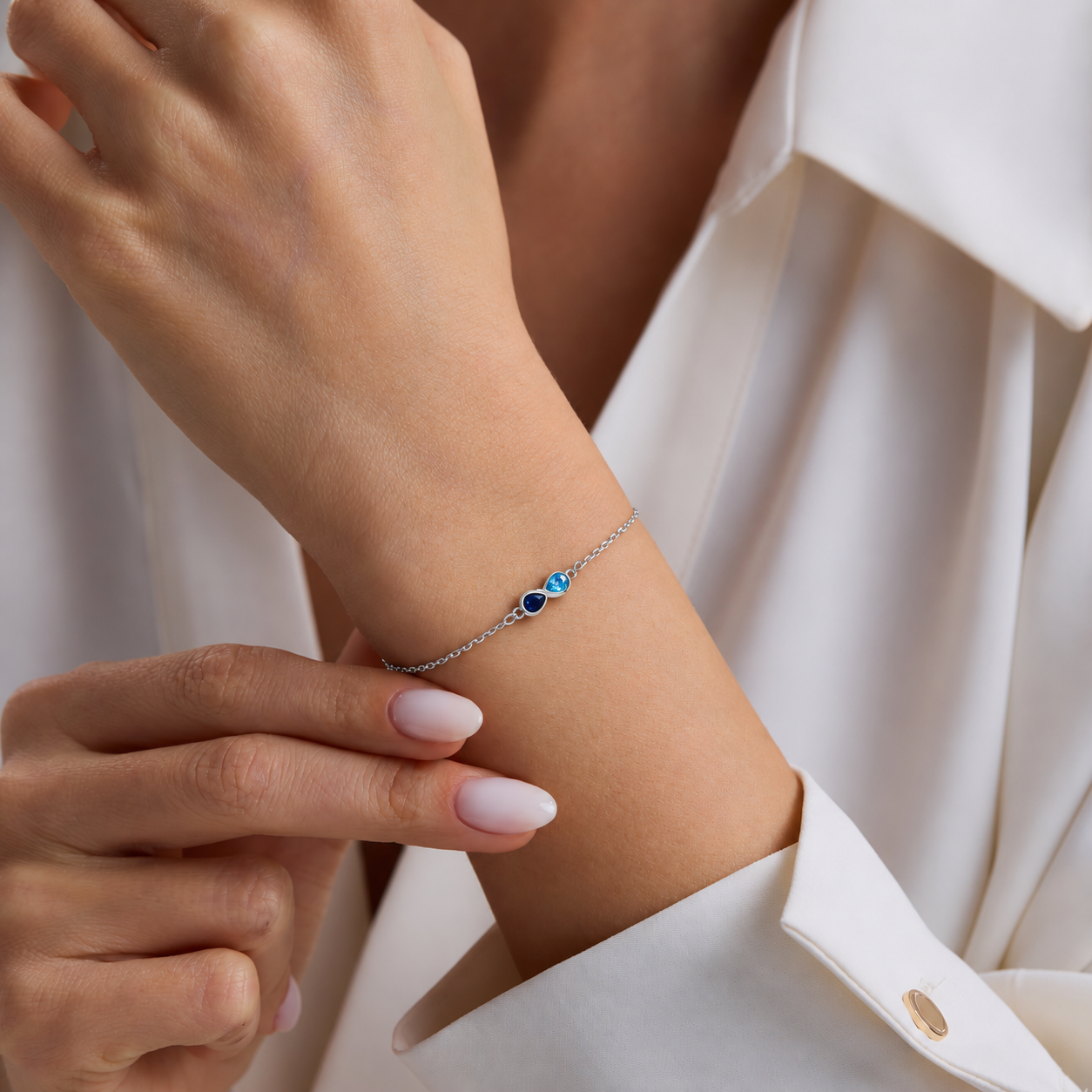Custom dual birthstone bracelet in sterling silver, with navy and aqua teardrop stones worn on the wrist