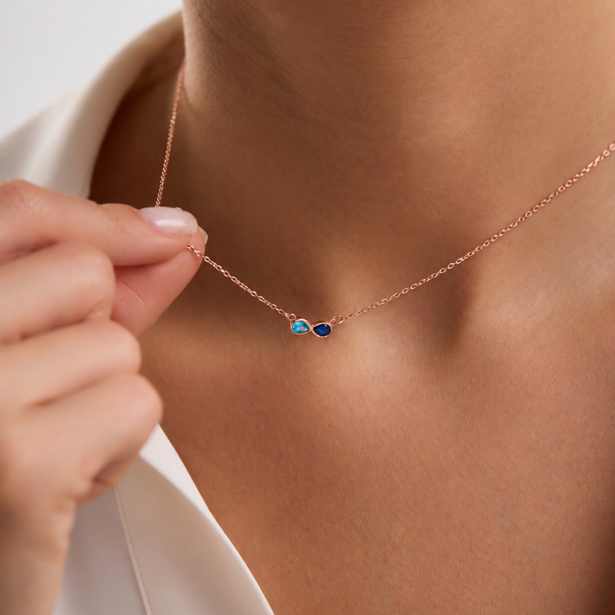 Custom dual birthstone necklace in rose gold with light blue and navy pear-shaped gemstones, worn on the neck