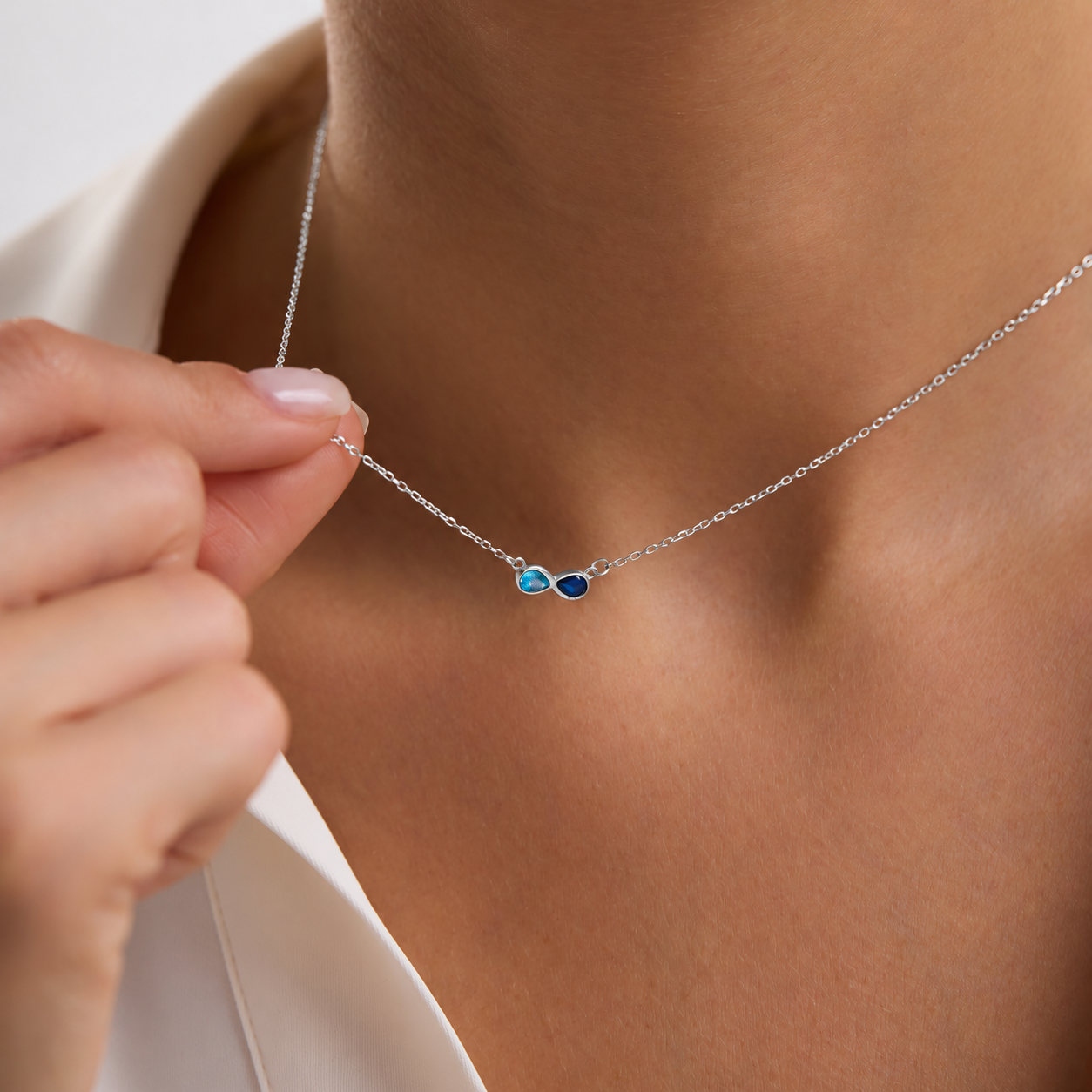 Custom dual birthstone necklace in sterling silver with light blue and navy pear-shaped gemstones, worn on the neck