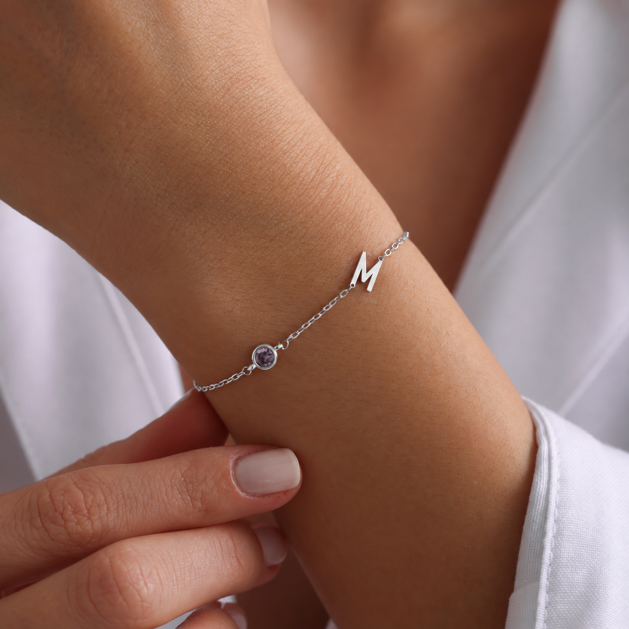 Sterling silver M initial birthstone bracelet with a round purple gemstone, worn on a wrist