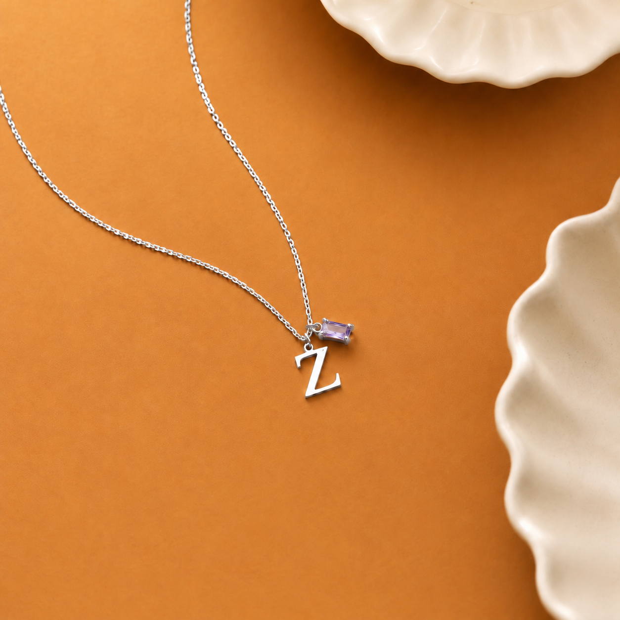 14K solid white gold Z initial necklace with a purple baguette birthstone on an orange surface beside ceramic dishes