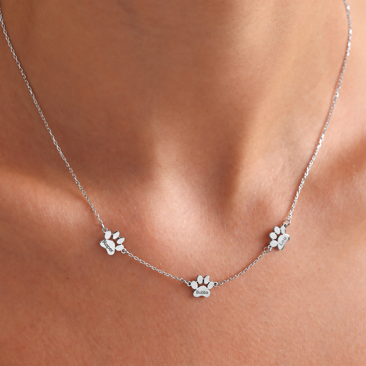Sterling silver pet memorial necklace with three personalized paw charms, worn close-up