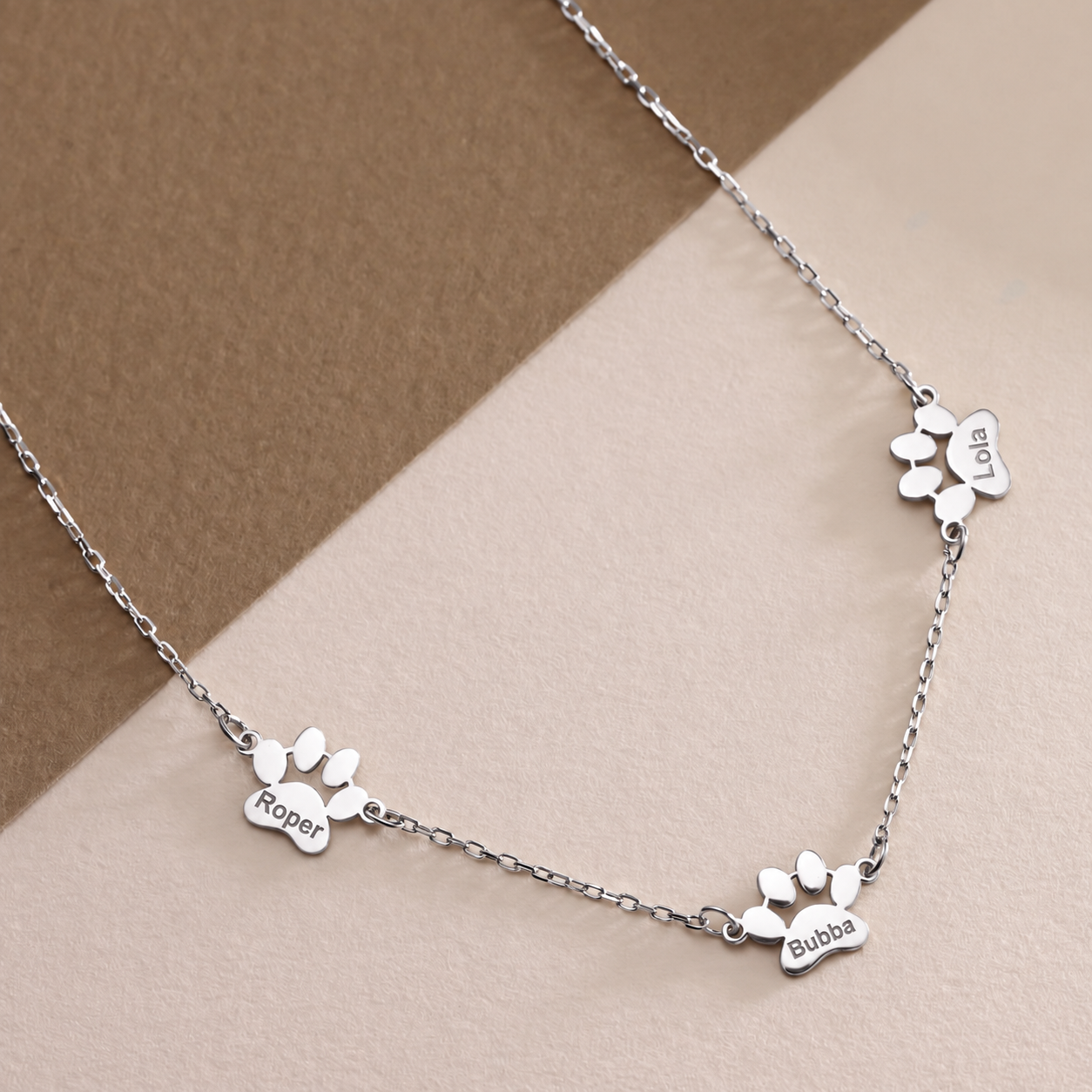 14K solid white gold pet memorial necklace with paw charms engraved Roper, Bubba and Lola on beige and taupe surfaces