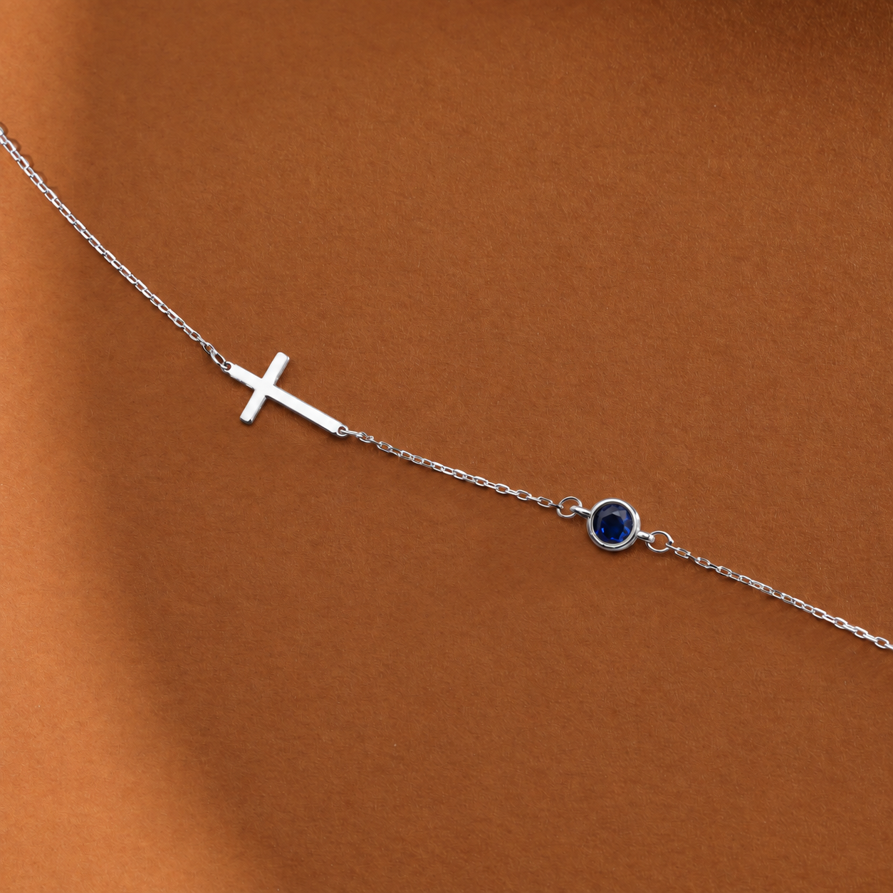 14K solid white gold sideways cross bracelet with a round blue birthstone on an orange-brown surface