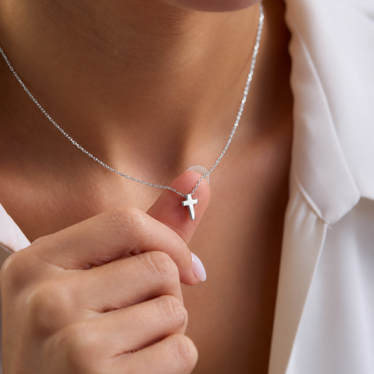 Dainty cross pendant necklace in sterling silver, held on a fingertip