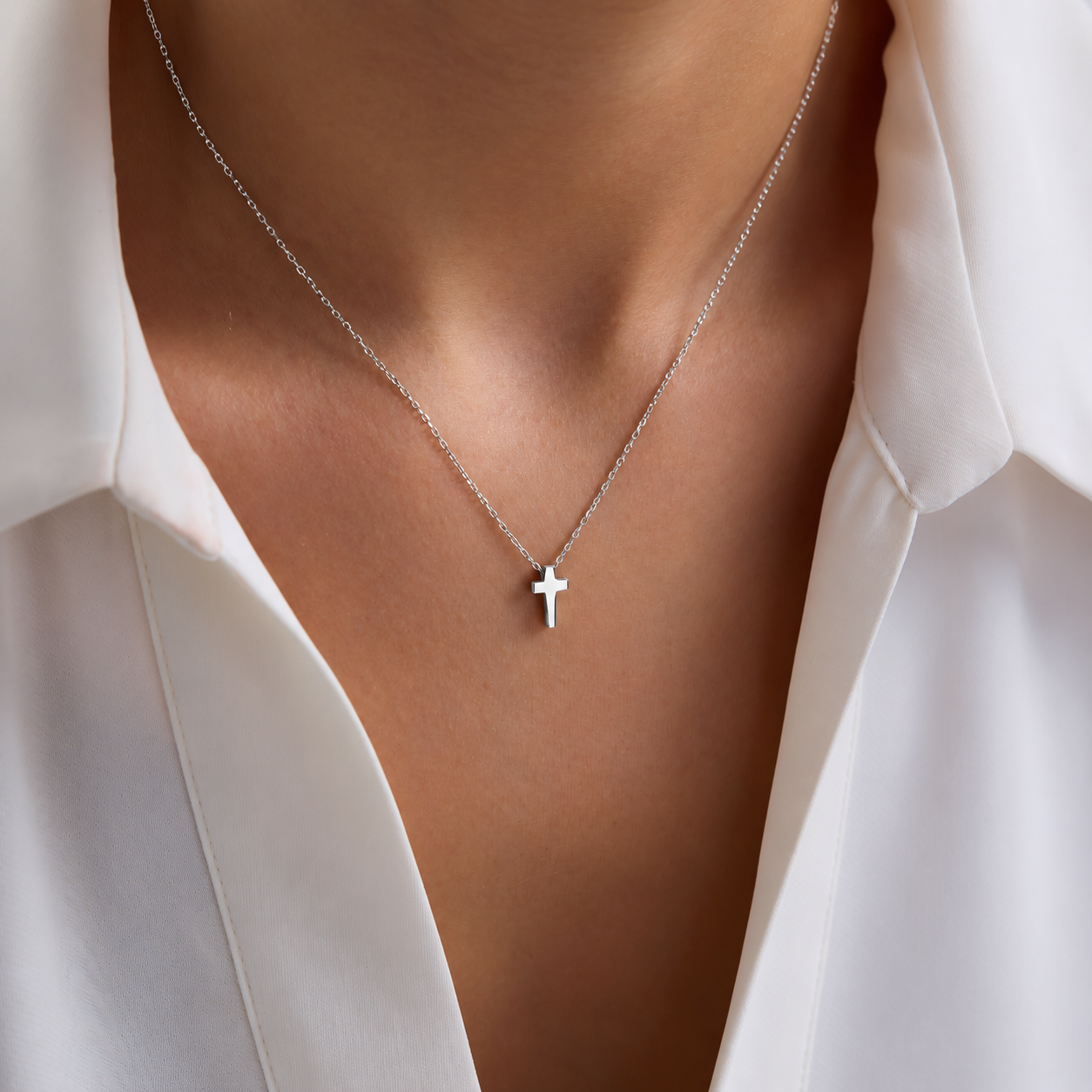 Dainty cross pendant necklace in solid white gold, worn with a white shirt