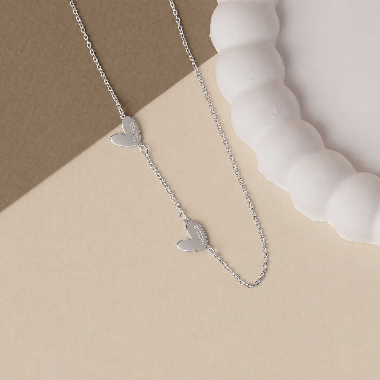 Engraved family heart necklace in solid white gold, with Carrie and Jessica charms on a cream background