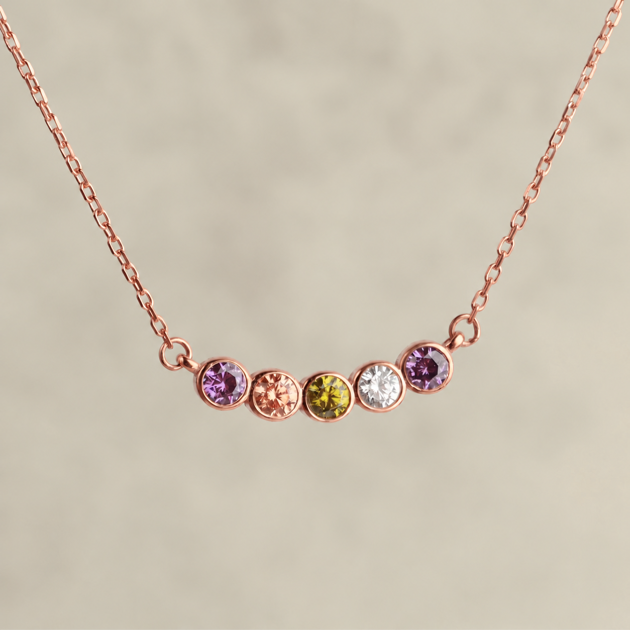 Family birthstone necklace in rose gold with five colourful gemstones, close-up on a neutral background