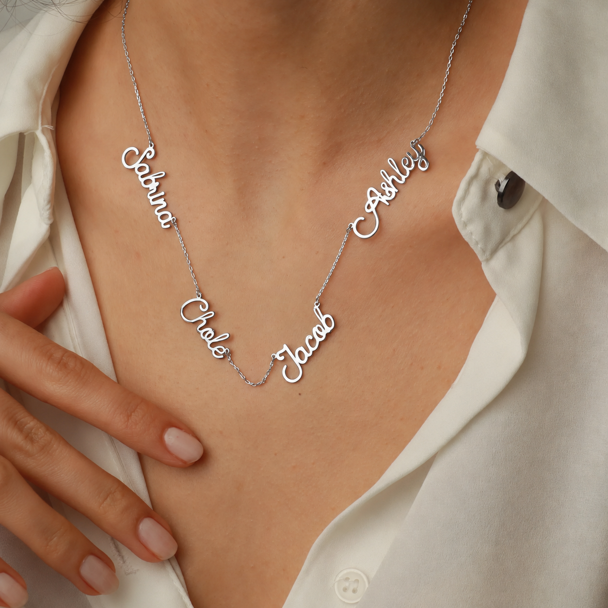 Family name necklace in 14K solid white gold, featuring four script name stations on a fine chain, worn with a white blouse.