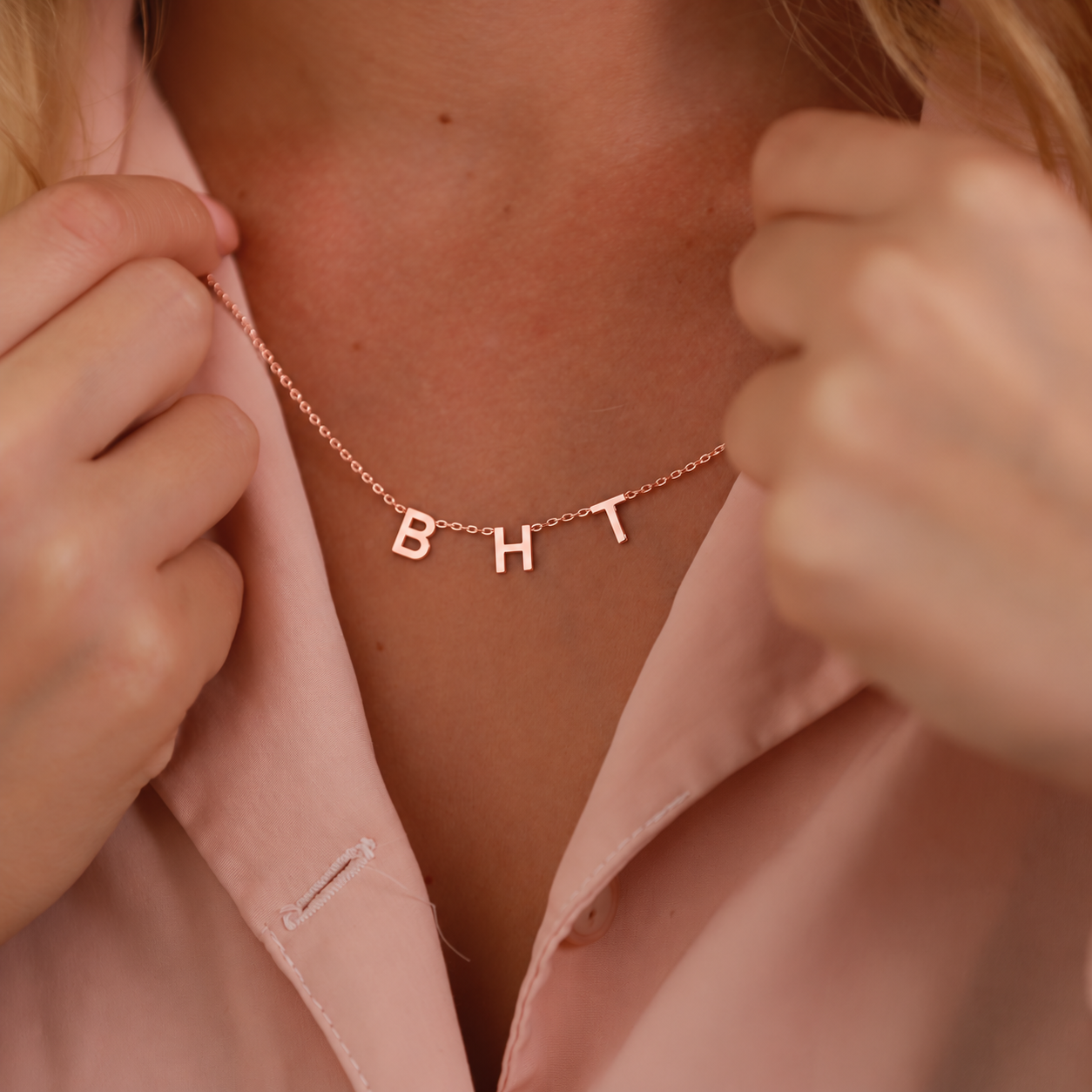 Initial letter necklace in 14K rose gold filled with B H and T charms, worn with a pink shirt