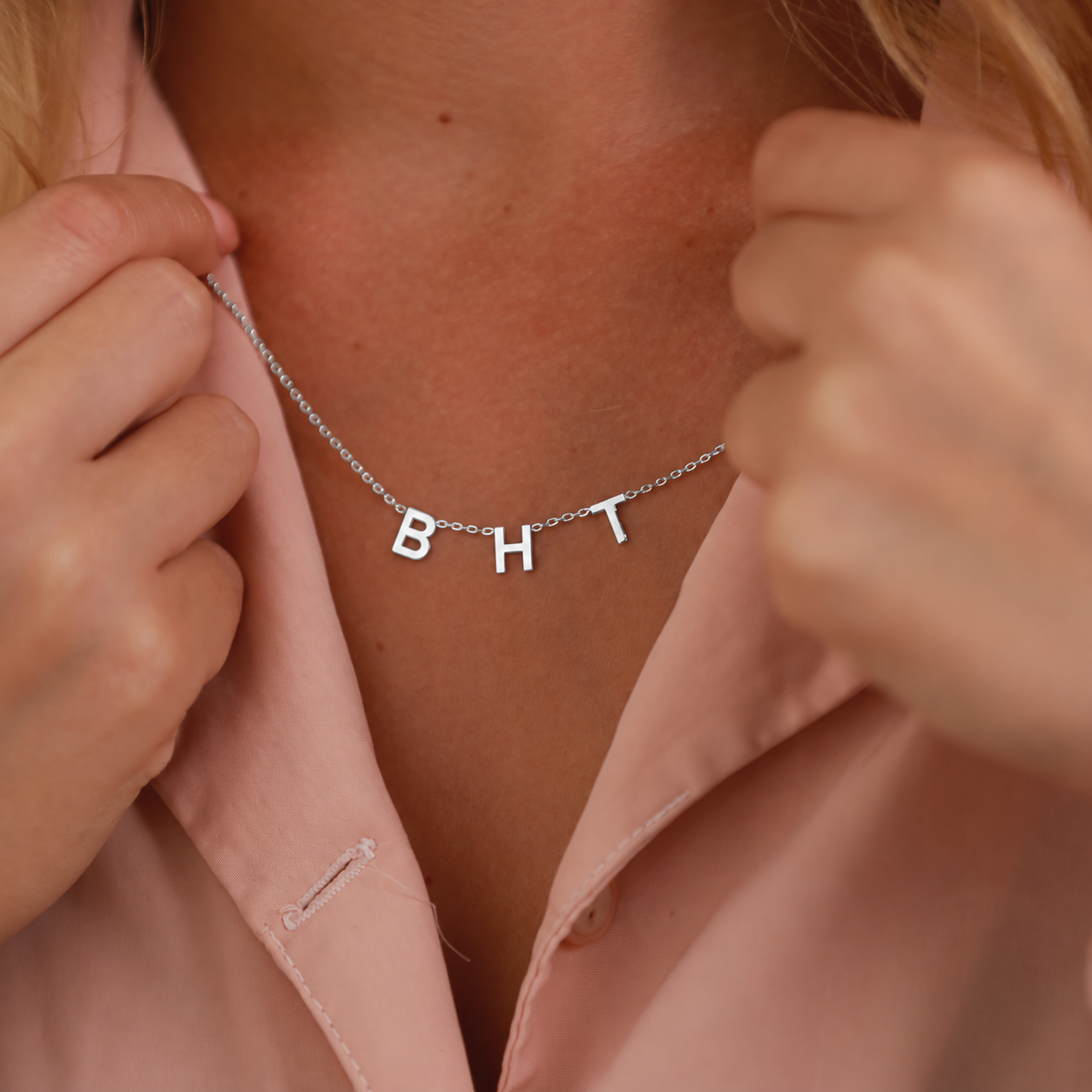 Initial letter necklace in sterling silver with B H and T charms, worn with a pink shirt