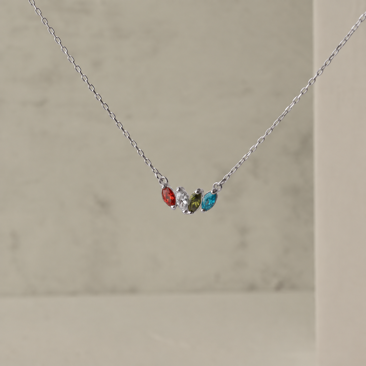 Mom's birthstone necklace in solid white gold with four colourful marquise gemstones, close-up on a neutral background