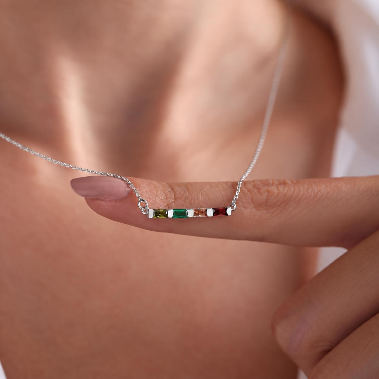 Personalized birthstone necklace in sterling silver with four colourful baguette gemstones, held on a finger
