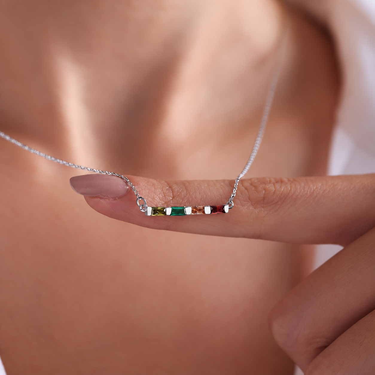 Personalized birthstone necklace in solid white gold with four colourful baguette gemstones, held on a finger