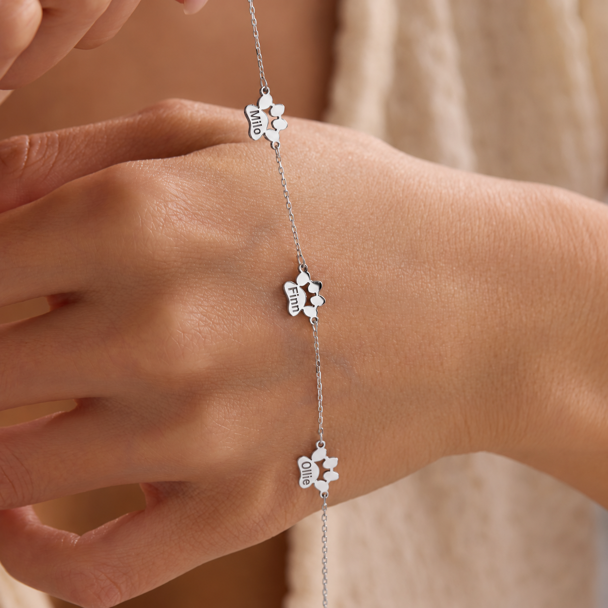 Personalized pet paw bracelet in 925 sterling silver with three paw-shaped stations engraved Milo, Finn and Ollie, displayed across a hand.