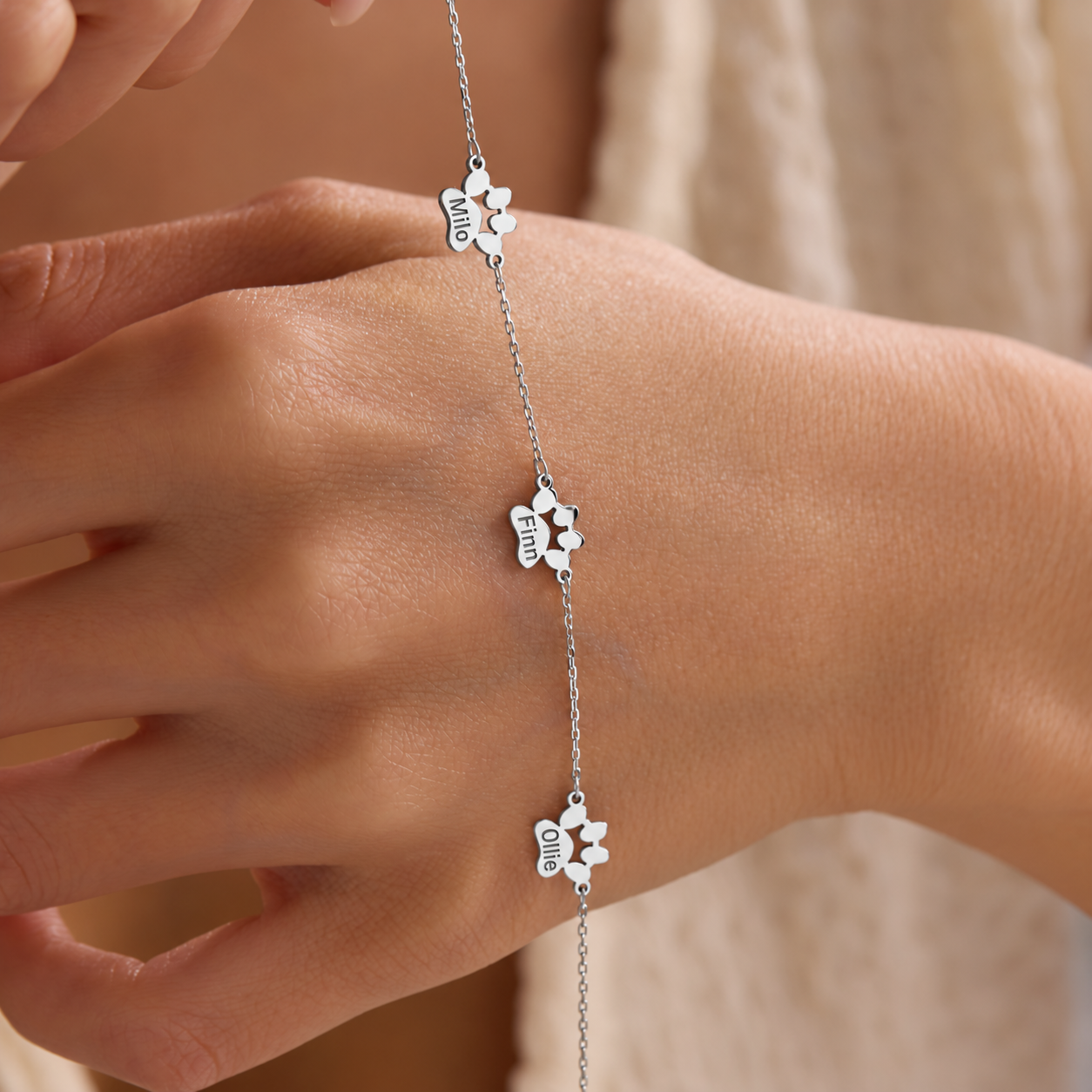 Personalized pet paw bracelet in 14K solid white gold with three paw-shaped stations engraved Milo, Finn and Ollie, displayed across a hand.
