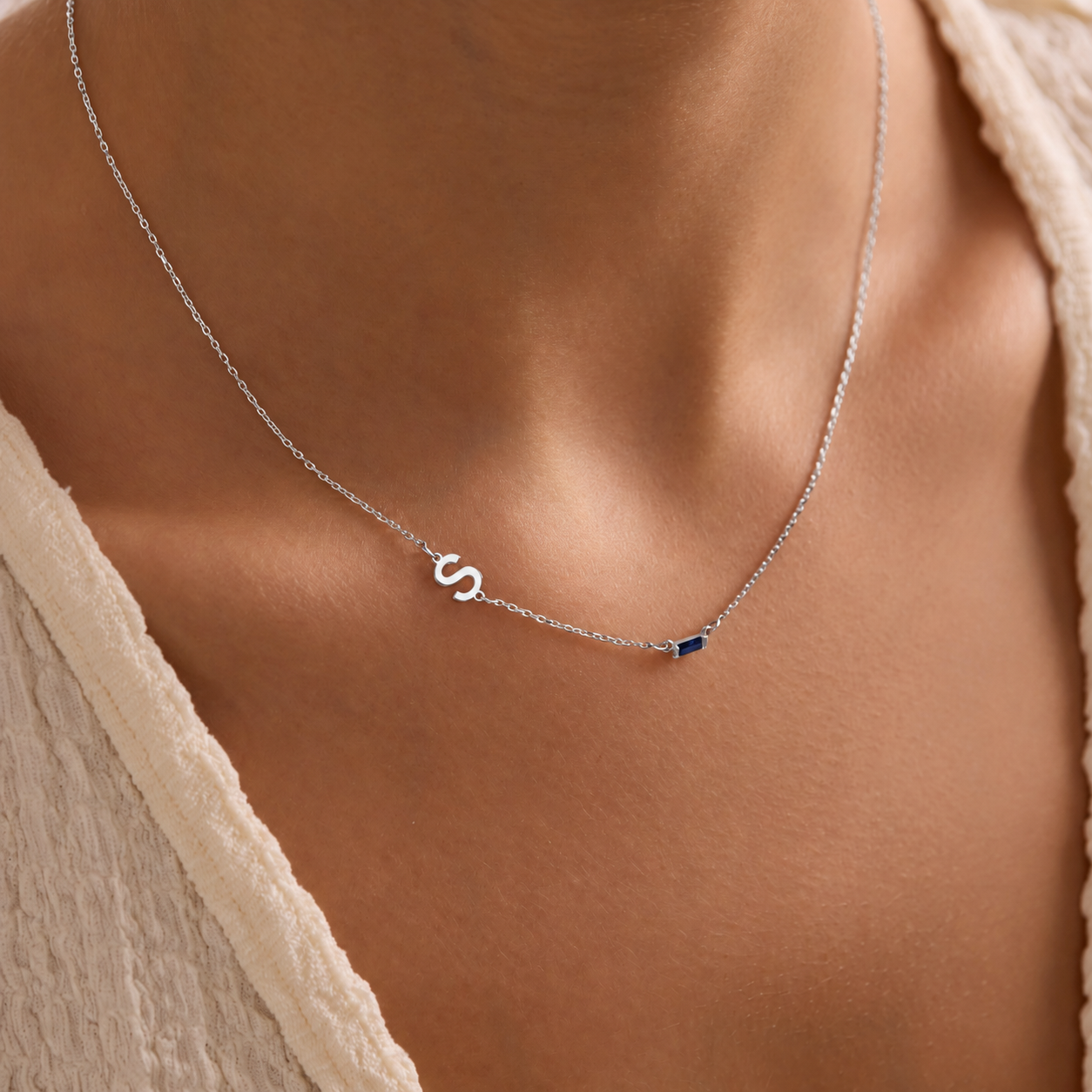 Sideways initial birthstone necklace in sterling silver, with an S initial and navy rectangular gemstone worn with a cream top