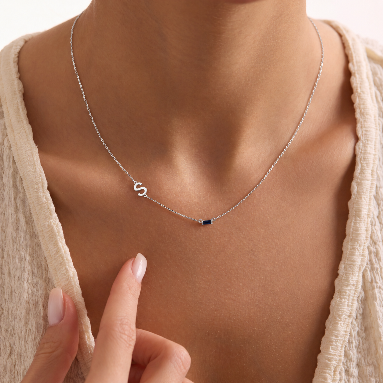 Sideways initial birthstone necklace in solid white gold, with an S initial and navy rectangular gemstone worn with a cream top