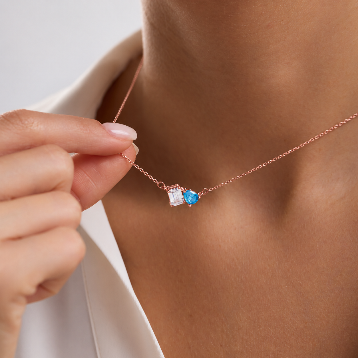Toi et Moi birthstone necklace in rose gold with clear rectangular and blue pear-shaped gemstones, worn on the neck