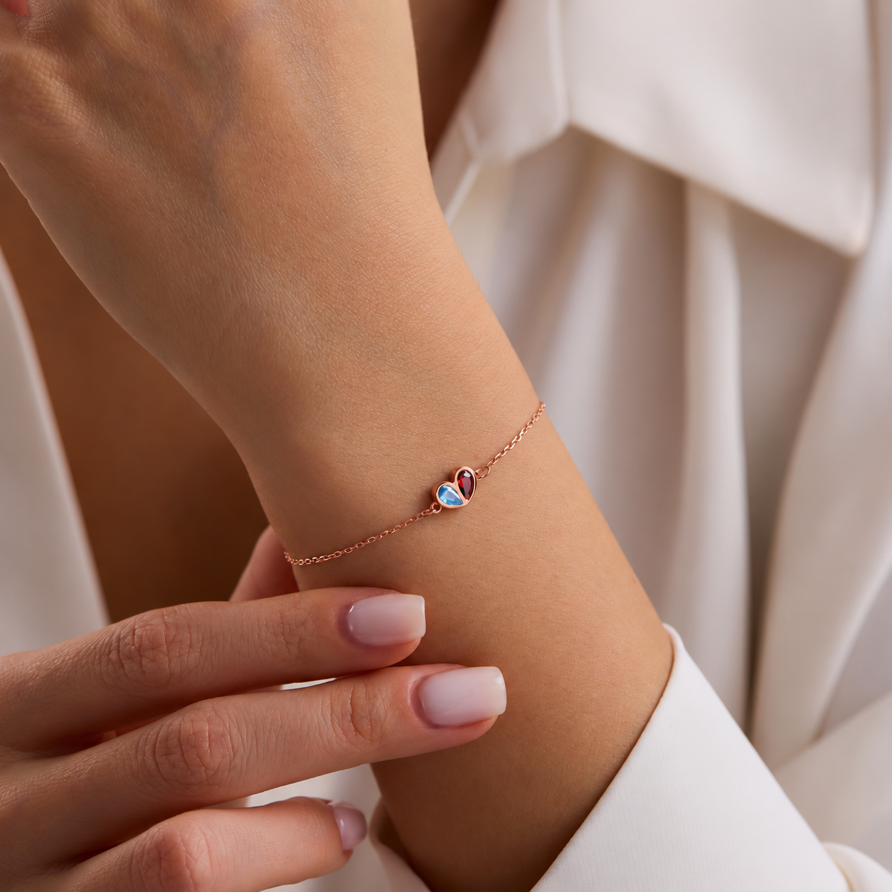 Two birthstone heart bracelet in rose gold with blue and red gemstones, worn on the wrist