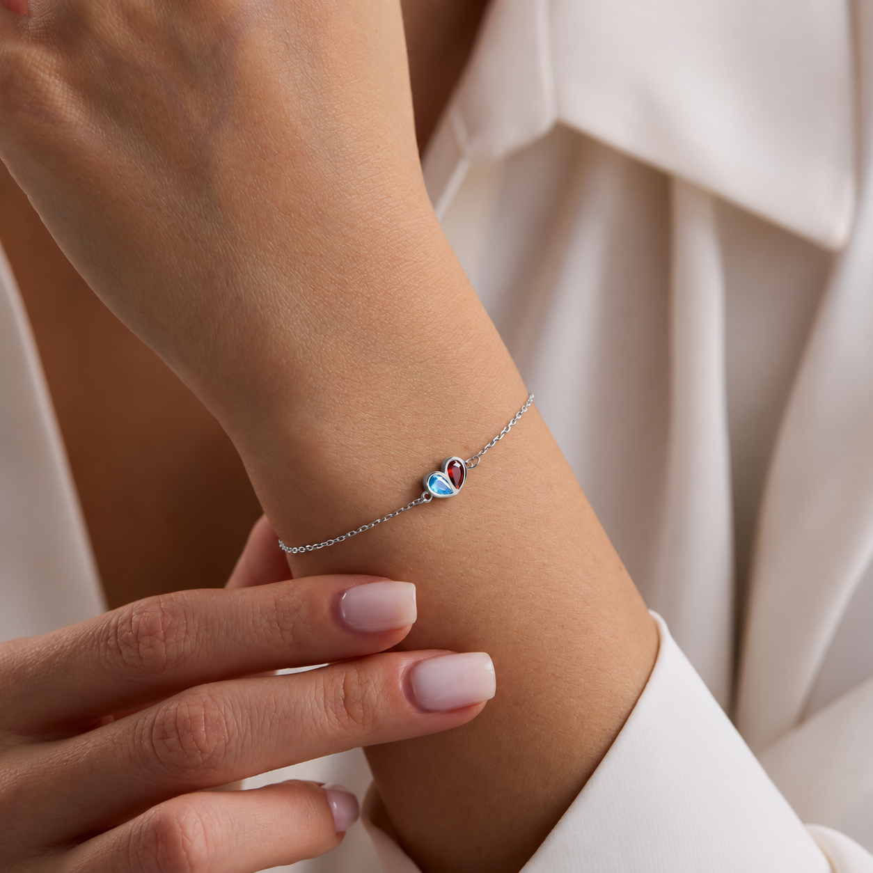 Two birthstone heart bracelet in sterling silver with blue and red gemstones, worn on the wrist