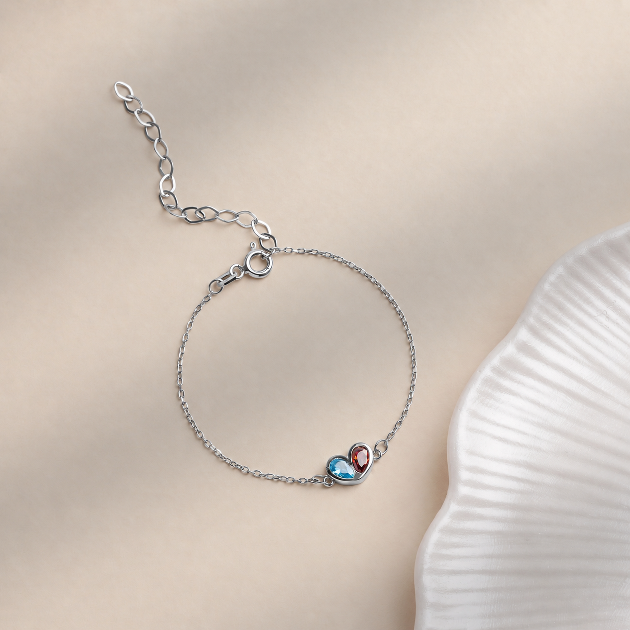 Two birthstone heart bracelet in solid white gold with blue and red gemstones, clasp and extender chain on a cream background