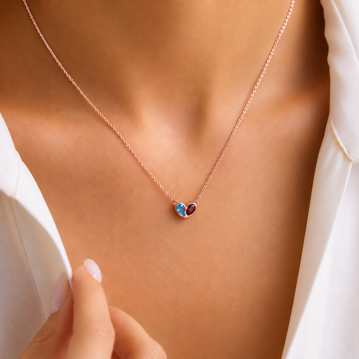 Two birthstone heart pendant necklace in rose gold with blue and red gemstones, worn with a white shirt