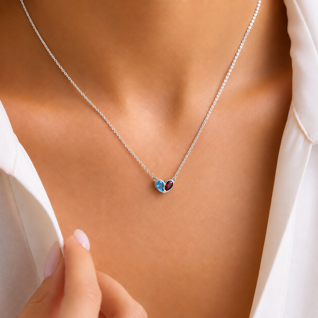 Two birthstone heart pendant necklace in sterling silver with blue and red gemstones, worn with a white shirt